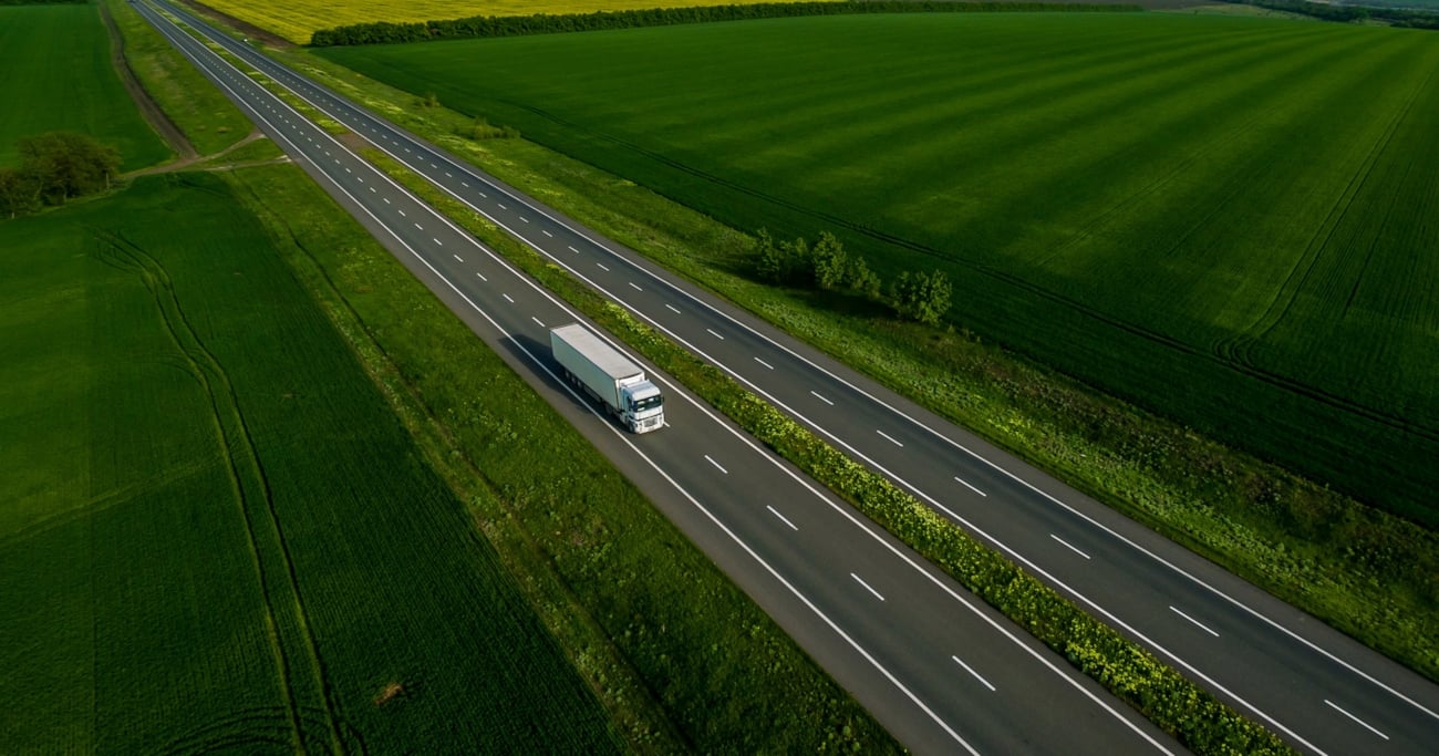 dronefoto av lastebil langs tom motorvei grønne trær