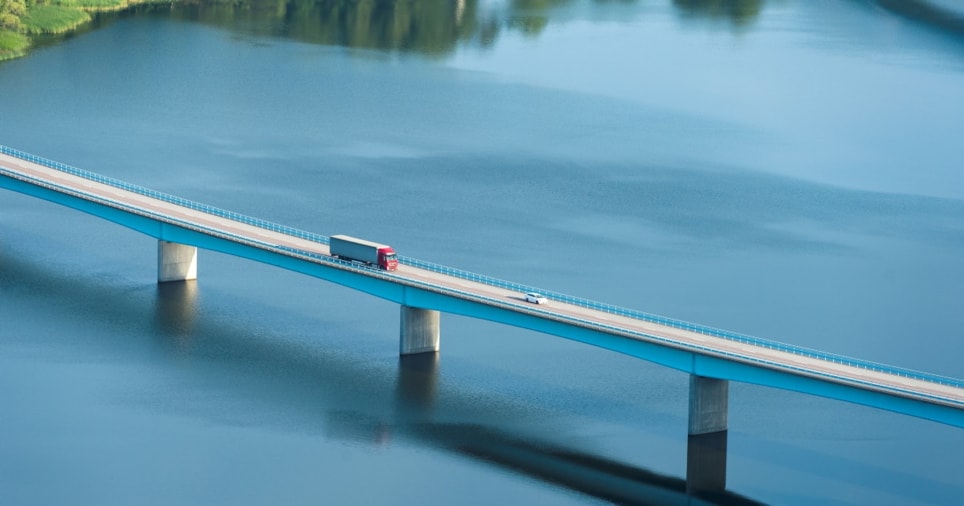 lastebil som kjører over bro over elv. dronefoto
